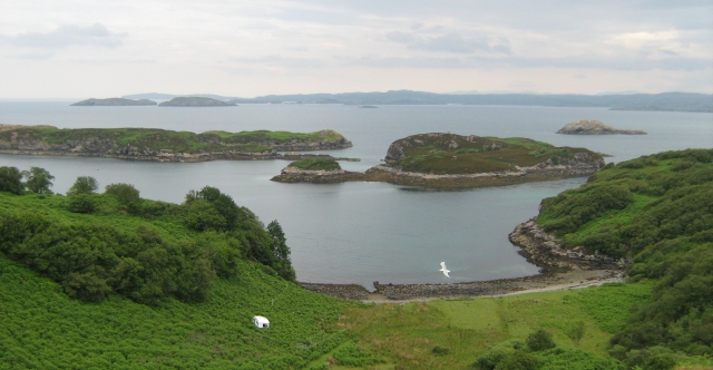 the view from drumbeg viewpoint.  islands in the sea and a steep hill to the shore, and a caravan in the bushes
